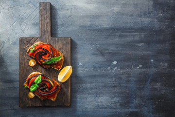 Black board with appetizer with aubergines and bell peppers.