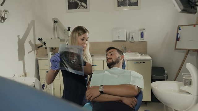 A female dentist shows the patient's x-ray of the teeth and discusses their further treatment