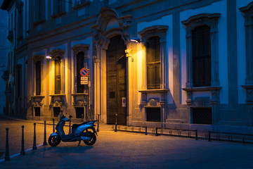 Serene view of a small motorbike parked in an alley in Milan, Italy, at night, under the warm...