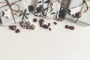 modern christmas flat lay composition. stylish wrapped presents with ornaments and  cones anise on rustic white wood, space for text, top view. seasonal greetings. happy holidays, xmas card