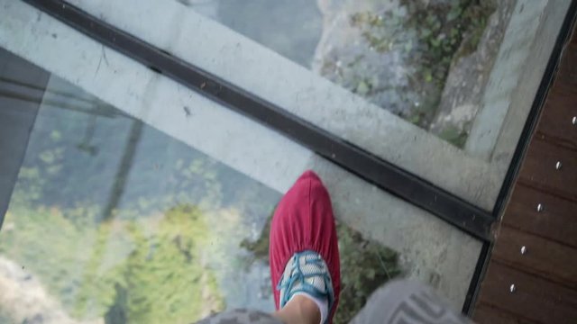 POV view of the legs in red boot covers walking along sgass sky walk at Tianmenshan National Park in China