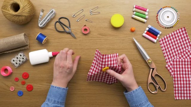 Overhead Shot Of Woman Sewing Yellow Button On Plaid Cloth