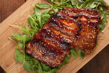 Closeup of pork ribs grilled with BBQ sauce and caramelized in honey on a bed of arugula. Tasty snack to beer on a wooden Board for submission on the old wooden background. Top view