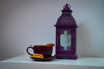 a white coffee table on which stands a cup and a richly decorated lantern