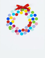 Colorful dots arranged into a Christmas wreath shape on a light background with a red bow on top. Fun, cheerful image.