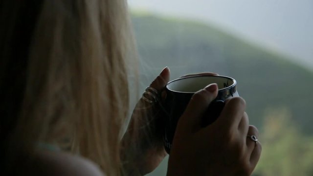 Young beautiful woman enjoys her morning tea looking at the mountains and rice fields in famous Ping An Village, Longji,China. Freedom,Calmness and relax concept.Attractive girl holding cup of coffee