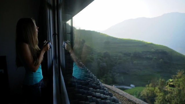Young beautiful woman enjoys her morning tea looking at the mountains and rice fields in famous Ping An Village, Longji,China. Freedom,Calmness and relax concept.Attractive girl holding cup of coffee