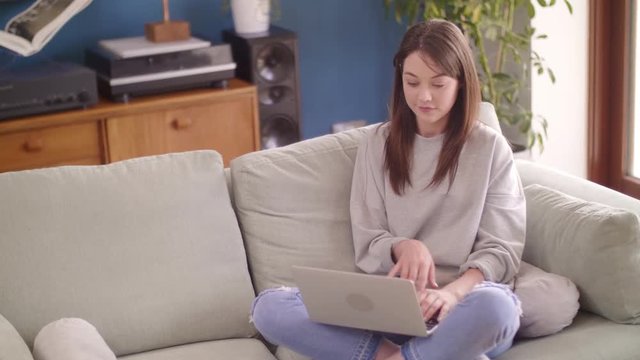 Beautiful Female Blogger Using Laptop While Sitting On Sofa At Home