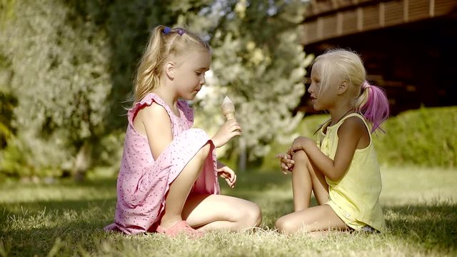 Two little cute girls, sisters sitting on the grass on the lawn in the summer