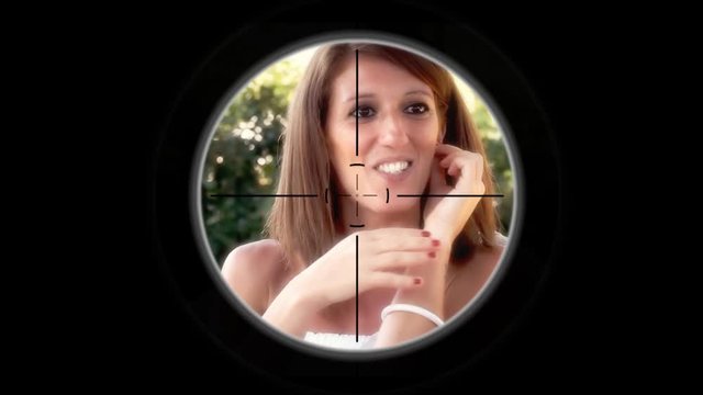 A sniper scope pointing at a chatty garrulous woman talking to her friends, smiling, looking interested. Sunny day, outdoors.
