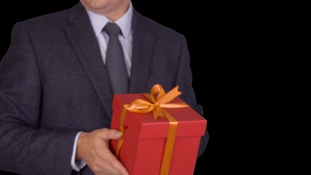 Caucasian businessman hold and give red gift box. From unfocus to focus motion. Adult man in classic business suit hold red gift box. Alpha channel chroma key transparent background. Locked down.