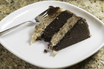 piece of German chocolate cake on a square white plate with a fork in the cake