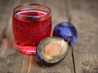 Two ripe plums and a glass of fresh homemade plum aperitif on a wooden rustic table.
