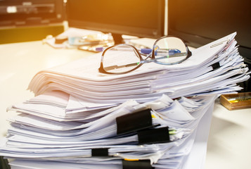 Glasses placed on Unfinished documents stacks of paper files on computer desk for report , piles of...