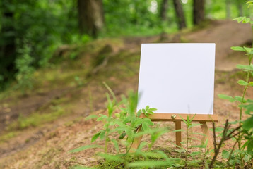 Painter workplace mockup. Blank template for sketch, hand drawn projects. Canvas on easel. Easel in the forest, with white space. Pure white canvas on a background of a landscape