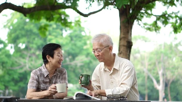 asian senior couple drinking coffee in morning beautiful park