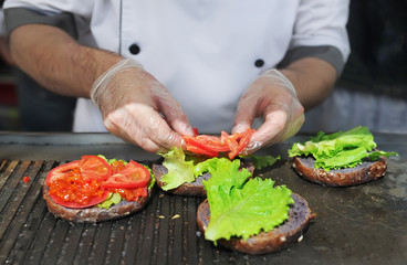 The cook preparing burger adding the tomato. Ingredients for preparation of hamburgers.