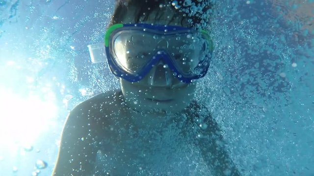 Boy jump in swimming pool dive and looking at the camera, waving hands