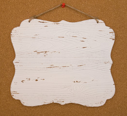 A white wooden board haning on a cork board