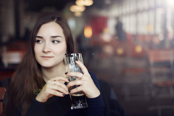 Beautiful girl drinking beer from the glass cup in bar. Girl tasting beer in brewery in Prague. Czech Republic.