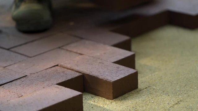 Closeup of a man setting brick pavers into place in a herringbone pattern.