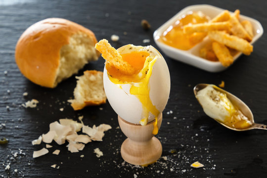 Soft boiled egg in a wooden egg cup, a piece of bread, toast-crackers. eggshell on a black table. food with crumbs