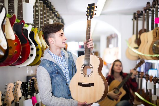 teenage customers deciding on suitable acoustic guitar in guitar shop