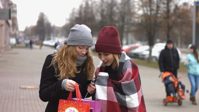 Two girls after the festive shopping consider the gifts.
Slow motion. Two young pretty girls stand on the street and holding bags with shopping.