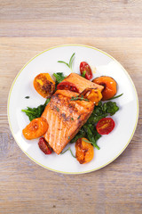 Salmon fillet with spinach and tomatoes on white plate on rustic wooden background. Overhead, top view