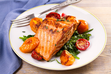 Salmon fillet with spinach and tomatoes on white plate on rustic wooden background