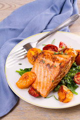 Salmon fillet with spinach and tomatoes on white plate on rustic wooden background