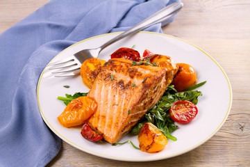 Salmon fillet with spinach and tomatoes on white plate on rustic wooden background