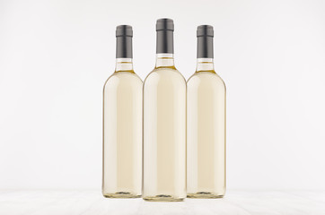 Three transparent wine bottles with white wine on white wooden board, mock up. 
