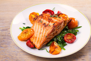 Salmon fillet with spinach and tomatoes on white plate on rustic wooden background