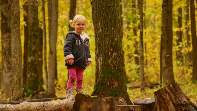 Child in the autumn forest. A girl is jumping from a hemp to a stump.