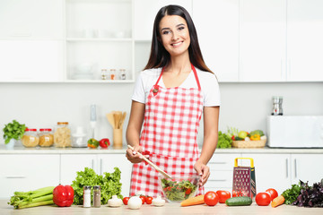 Beautiful young woman cooking salad in the kitchen