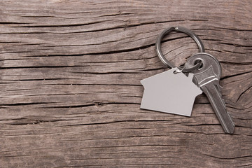 Key and keychain in the shape of a house on a wooden background. Copy space for text