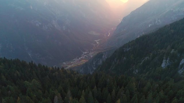 Aerial view flying over forest at dawn towards foggy canyon lit up by the sun in Italy.