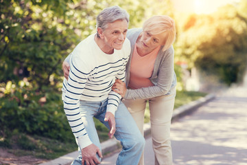 Care and support. Nice pleasant caring woman standing near her husband and helping him to walk while being on a walk