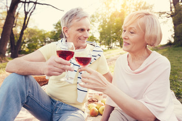 Many years together. Delighted positive aged couple sitting together and drinking wine while celebrating their anniversary of wedding