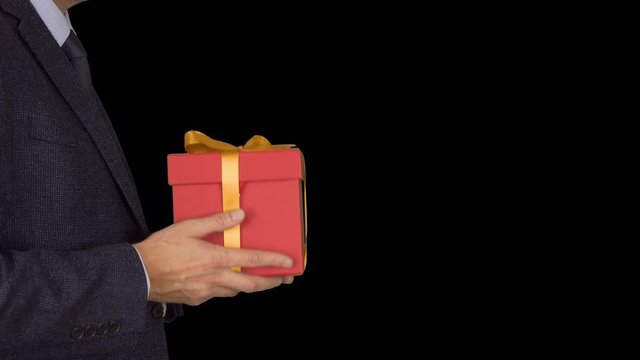 Caucasian businessman hold and give red gift box. From unfocus to focus motion. Adult man in classic business suit hold red gift box. Alpha channel chroma key transparent background. Locked down. CU.