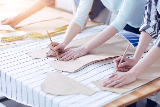 Start working. Three attentive tailors outlining the sewing pattern of a fashionable summer dress