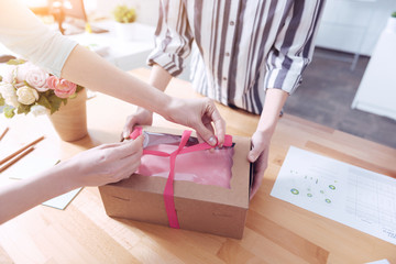 Sweet morning. Pair of women tying a pink ribbon on a gift box for their regular client