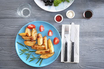 Composition with plate of baked rosemary potatoes on wooden table