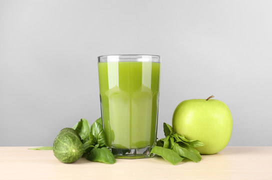 Green juice in glass and ingredients on table