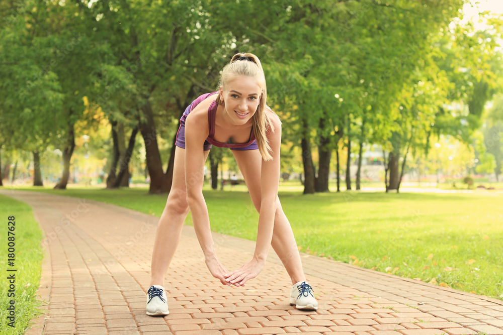 Wall mural young woman stretching in park