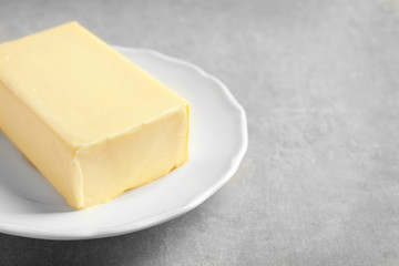 Plate with block of butter on grey background