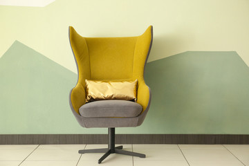 Comfortable armchair with pillow near color wall