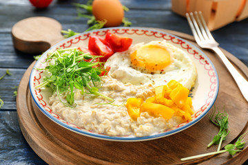 Plate with oatmeal porridge, fried egg and garnish on wooden board