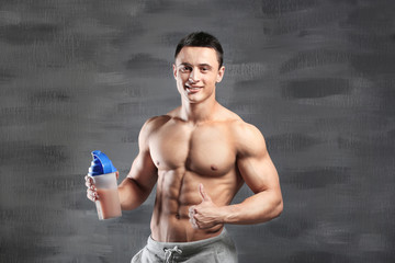 Sporty young man with protein shake on gray background